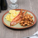A Libbey terracotta stoneware plate with bacon, eggs, and toast on it on a table.
