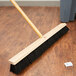 A Carlisle Flo Pac 24" push broom head with black bristles on a wood surface.