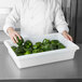 A chef holding a Rubbermaid white food storage container of green peppers.