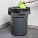A hand throwing a green lid into a gray Continental 55 gallon trash can.