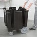 A person pushing a large black Cambro dish caddy.