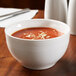 A white Libbey porcelain bouillon cup filled with tomato soup on a table.