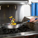 A hand using a Vollrath Wear-Ever blue handled frying pan to cook vegetables.