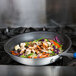 A Vollrath Wear-Ever aluminum non-stick fry pan filled with food on a stove.