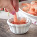 A hand dipping a shrimp into a white Carlisle ramekin of sauce.