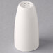 A Libbey ivory porcelain pepper shaker with holes on a gray surface.