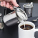 A person using a Thunder Group stainless steel server to pour milk into a cup of coffee.