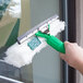 A hand holding a Unger green and white Visa Versa 10" window squeegee with a green and white cleaning pad to clean a window.