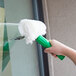 A hand using a green and white Unger Visa Versa window squeegee with a green handle to clean a window.
