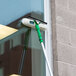 A Unger Visa Versa window squeegee with a green and white mop attached to it being used on a window.
