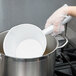 A gloved hand using a Vollrath aluminum dipper to pour liquid into a pot.