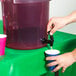 A person pouring water into a cup from a Carlisle purple beverage dispenser.