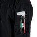 A person wearing a Mercer Culinary black chef jacket with a phone and pens in the pocket.