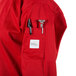 A person wearing a red Mercer Culinary cook jacket with a pen and sticker in the pocket.