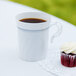 A white plastic coffee cup with silver accents filled with coffee next to a cupcake.