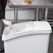 A person in gloves uses a plastic lid to cover a Baker's Mark ingredient bin.