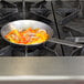 A Matfer Bourgeat carbon steel fry pan with vegetables cooking on a stove.