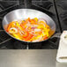 A Matfer Bourgeat carbon steel fry pan with vegetables cooking in it.