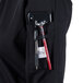 A person wearing a Mercer Culinary Millennia black chef jacket with a phone and tools in the pocket.