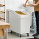 A white slant top mobile ingredient storage bin with a sliding lid and scoop, designed for bulk storage in kitchens.