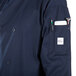 A person wearing a Mercer Culinary Millennia navy chef jacket with pockets and a pocket full of pens.