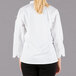 A woman wearing a Mercer Culinary white long sleeve chef jacket with cloth knot buttons.