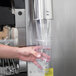 A hand pressing a plastic cup into a Vollrath cup dispenser on a hospital cafeteria counter.