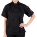 A woman wearing a black Mercer Culinary chef jacket with a pen in the pocket.