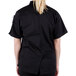 A woman wearing a Mercer Culinary Millennia black chef jacket with black cloth knot buttons.