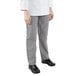 The legs of a person wearing Mercer Culinary Millennia Women's Houndstooth chef pants, a white coat, and black shoes.