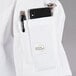 A white Mercer Culinary Millennia chef jacket with a pocket holding a cell phone and pen.