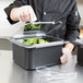 A person in gloves using tongs to put food into a Carlisle Clear Polycarbonate Food Pan with a lid.