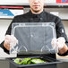 A man holding a Carlisle clear plastic food pan lid on a clear plastic tray filled with salad.