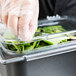 A person in plastic gloves using a Carlisle Coldmaster food pan lid with 2 handles to cover a salad in a plastic container.
