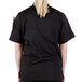 A woman wearing a Mercer Culinary Millennia black short sleeve chef jacket over a black shirt.