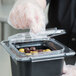 A plastic gloved hand uses a Carlisle Coldmaster food pan lid to cover a container of olives.