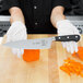 A person in white gloves using a Mercer Culinary Renaissance® chef's knife to slice an orange bell pepper.