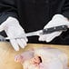 A person in white gloves using a Mercer Culinary Renaissance flexible boning knife to cut raw chicken.