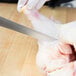 A person using a Mercer Culinary Renaissance flexible boning knife to cut a chicken leg.