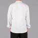 The back of a person wearing a Mercer Culinary white chef jacket with blue piping.