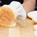 A person using a Mercer Culinary bread knife to cut a bread roll.