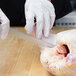 A gloved hand using a Mercer Culinary Renaissance stiff boning knife to cut a raw chicken.