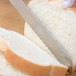 A Mercer Culinary Renaissance bread knife cutting a piece of bread.