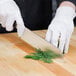 A person in white gloves uses a Mercer Culinary Renaissance Nakiri Knife to cut greens on a wooden cutting board.