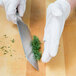 A person in white gloves using a Mercer Culinary Renaissance Nakiri knife to cut a vegetable.