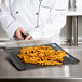 A person in a white chef's coat using a Baker's Mark black mesh screen to cook french fries.