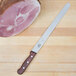A Victorinox roast beef carving knife with a rosewood handle on a cutting board next to a piece of meat.