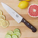 A Victorinox chef knife next to sliced lemons and limes on a wooden cutting board.