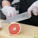 A person using a Victorinox chef knife to cut a grapefruit.