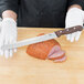 A person in white gloves using a Victorinox 10" Granton Edge Slicing / Carving Knife to slice ham.